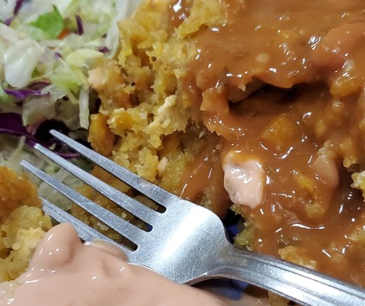 A close view of mofongo with sauce, salad, and a fork.
